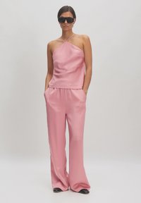Roze satijnen haltertop met een losse pasvorm, gecombineerd met bijpassende roze broeken met zijzakken en wijde pijpen. Accessoires omvatten zwarte zonnebril.