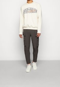 Beige sweatshirt with "COUTURE" graphic, paired with dark gray cargo pants featuring side pockets. Styled with white sneakers.