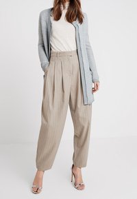 Ljust grått stickat cardigan, off-white topp, beige randiga byxor och silverfärgade högklackade sandaler; avslappnad passform med veckdetaljer.