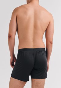 Schwarze Boxershorts aus glattem Stoff, mit einem weichen elastischen Bund und dezentem Branding, von hinten gezeigt.