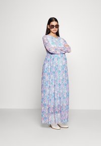 Maxikleid im Blumendesign mit blauen, pinken und weißen Farben. Lange Ärmel, runder Ausschnitt, fließender Stoff, kombiniert mit weißen Ankle-Boots.