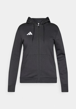 Crna dukserica s patentnim zatvaračem i kapuljačom s vezicama, izrađena od mekanog tkanja. Na prsima je bijeli adidas logo, a s prednje strane se nalaze dva džepa.