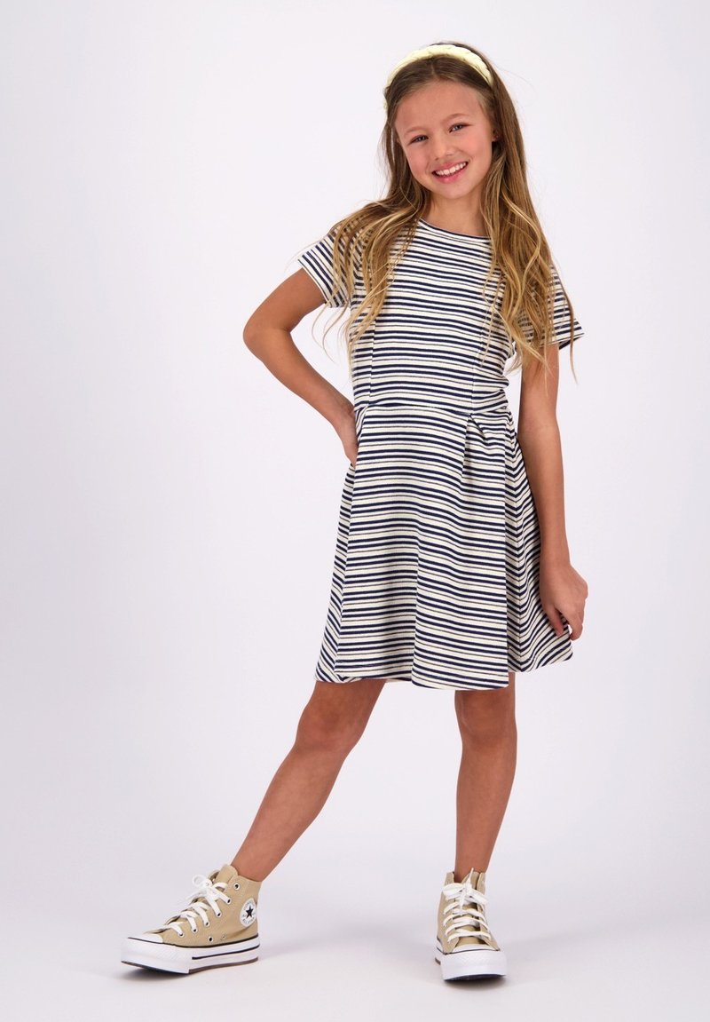 Gestreiftes Kleid in Marineblau und Weiß, mit kurzen Ärmeln und einem ausgestellten Rock. Kombiniert mit beigen High-Top-Sneakern. Einfaches, lässiges Design.