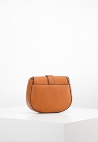 Brązowa skórzana torba na ramię o zaokrąglonym kształcie, z usztywnionym zapięciem na klapkę i subtelnymi akcentami szewskimi. Kompaktowy i minimalistyczny design.