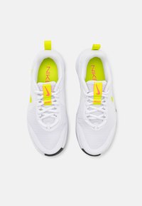 Hvite atletiske sko med mesh-overdel, gule detaljer og svarte såler. Har en lys rosa Nike-logo og polstret krage.