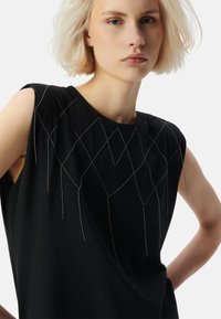 Top senza maniche nero con un design testurizzato e accenti in filo argentato che formano motivi geometrici sulle spalle e sul petto.