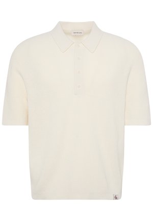 Polo en maille crème manches courtes avec patte de boutonnage et col, comprenant une petite étiquette logo à l'ourlet et une étiquette de marque à l’intérieur du col.