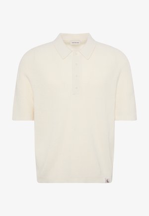 Polo en maille crème manches courtes avec patte de boutonnage et col, comprenant une petite étiquette logo à l'ourlet et une étiquette de marque à l’intérieur du col.