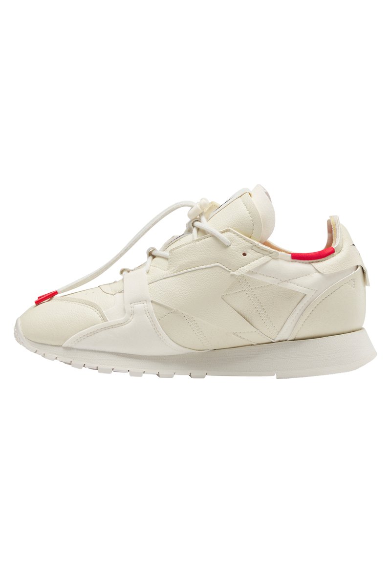 Chaussure avec une tige en cuir crème à finition texturée, accent rouge au niveau du talon, et une semelle en caoutchouc blanche. Design simple à lacets.