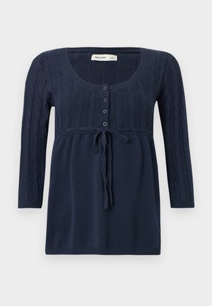 Gornji dio tamnoplave pletene majice s okruglim dekolteom, prednjim gumbima, uzorkom pletenice, vezicom u struku i dugim rukavima.