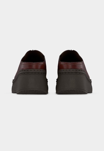 Ζευγάρι καφέ δερμάτινα παπούτσια με χοντρές μαύρες σόλες, εμφανιζόμενα από πίσω, σε λευκό φόντο.