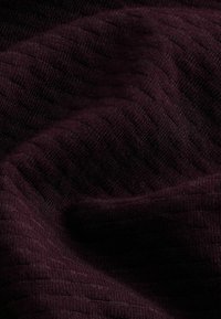 Tessut texturat de culoare burgundă închisă, cu o suprafață moale, în dungi. Materialul pare ușor elastic și țesut, creând o adâncime subtilă a modelului.