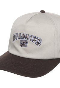 Grijze stoffen pet met een donkerbruine klep. Voorzien van het geborduurde "BILLABONG" logo in blauw en bruin. Gestructureerd ontwerp met een aansluitende achterkant.