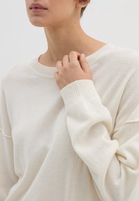 Pehmeä, kermaisen värinen villapaita, jossa on pyöreä pääntie, ribatut hihansuut ja rento malli. Materiaali vaikuttaa kevyeltä ja siinä on hienovarainen tekstuuri.