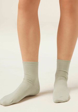 Béžové ponožky sahající ke kotníkům nošené na bosých nohou, zobrazené zepředu a ze strany na neutrálním pozadí.
