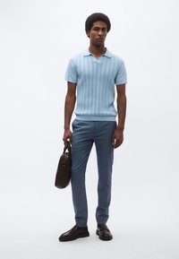 Ανοιχτό γαλάζιο πλεκτό πόλο με υφασμάτινο μοτίβο, συνδυασμένο με ραμμένο μπλε παντελόνι. Μαύρα δερμάτινα παπούτσια και καφέ τσάντα ώμου.