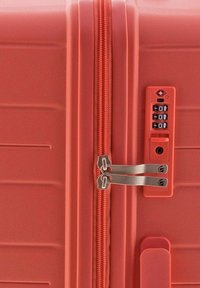 Valigia rigida di colore corallo con doppia cerniera, lucchetto approvato TSA e design minimalista. Presenta una superficie testurizzata con scanalature orizzontali.