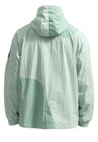 Licht mintgroene jas met capuchon, textuurstof en asymmetrisch ontwerp met contrasterende stof en gele stiksels.