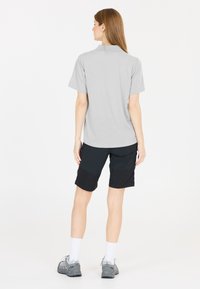 Grå kortärmad skjorta med avslappnad passform, tillsammans med svarta shorts med färgblockdesign. Modellen bär vita strumpor till mitt på vaden och grå skor.