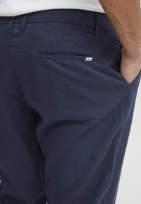 Pantaloni bleumarin dintr-un material ușor, având un buzunar pe spate și o etichetă mică a mărcii. Textură cu un finisaj plăcut și o croială confortabilă.