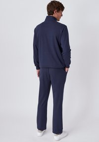Ensemble de survêtement en polaire marine avec un col haut, des manches longues et des poignets élastiques. Le pantalon fuselé dispose de poches latérales. Texture douce, design minimaliste.