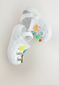 Sabots blancs décorés de diverses autocollants colorés, y compris des personnages de dessins animés et des icônes ludiques, présentés sur un fond clair.