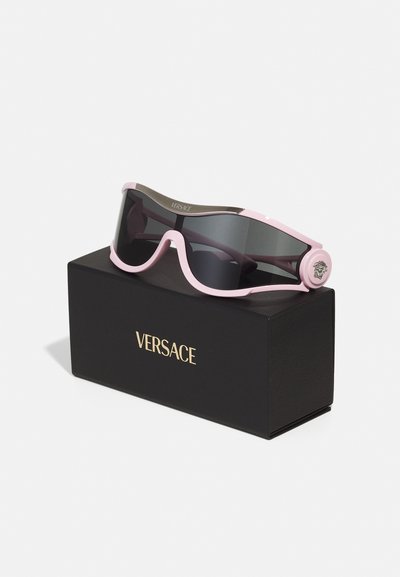 Pink and black sport sunglasses with a curved frame, dark lenses, and a metallic logo detail on the sides, displayed on a black box.
