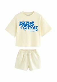 Lys gul bomulds sæt bestående af en boxy t-shirt med blå grafisk tekst og stribede shorts med elastisk talje.
