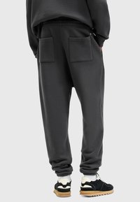 Mørkegrå sweatpants med elastisk talje, to baglommer og en afslappet pasform, parret med sort-hvide sneakers.