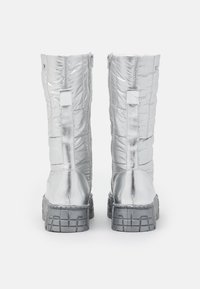 Botas plateadas hasta la rodilla con textura acolchada, acabado metálico y suela de goma gruesa. Presentan una cremallera trasera y acentos rectangulares.