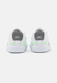 Nike shoes in white, featuring a gray heel tab, green accents on the sides, and textured white outsoles. Cushioned collar for comfort.