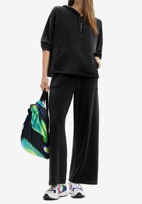 Sudadera negra de gran tamaño con un bolsillo frontal y capucha con cordón, combinada con pantalones negros de pierna ancha. Incluye una mochila de cordón con un diseño de tie-dye multicolor.