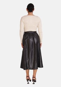 Schwarzer Leder-Midirock mit geraffter Taille, kombiniert mit einem eng anliegenden cremefarbenen, langärmeligen Ripptop. Optionale Schuhe mit einzigartigem Absatzdesign.