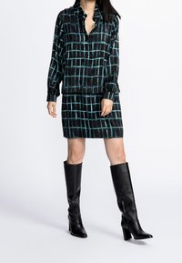 Set di blusa e gonna a fantasia nera e verde petrolio realizzato in tessuto morbido, abbinato a stivali neri in pelle con tacco alti fino al ginocchio.