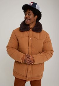 Casaco acolchoado castanho com gola de pelo falso macio castanho escuro, botões de pressão e punhos canelados. Design acolchoado quente com um corte descontraído.