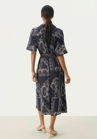Rochie midi bleumarin cu model paisley, mâneci scurte, talie definită cu cordon și o silueta fluidă. Material neted cu o textură moale.