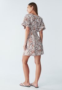 Kortærmet minikjole i brunt og hvidt zebra mønster, med en taljegathering og blødt, letvægtsstof. Kombineret med flade sandaler.