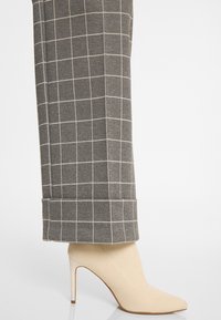 Beige pumps met een gestructureerd oppervlak, gecombineerd met grijze geruite wijde broek met witte rasterlijnen en een opgerold zoom.