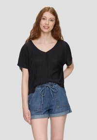 Schwarzes, plissiertes V-Ausschnitt-Oberteil kombiniert mit blauen Denim-Shorts mit elastischem Bund und umgeschlagenen Säumen.