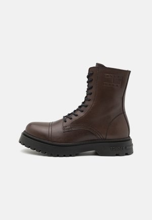 Bota de cuero marrón oscuro con cordones hasta el tobillo, suela gruesa negra con dibujo y el logotipo "Tommy Jeans" en relieve en el lateral y la suela.