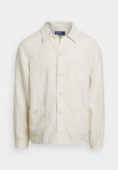 Light beige linen button-up shirt with a pointed collar, front pocket, and two lower pockets; textured fabric with a relaxed fit.