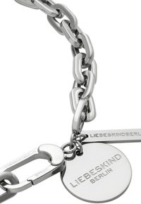 Silverkedja armband med stora länkar, en karbinhake och en rund tag med graverad text "LIEBESKIND BERLIN." Polerad yta.