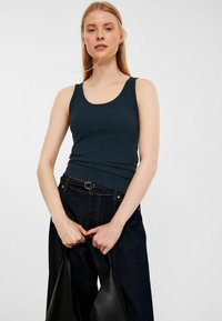 Dunkelblauer Tanktop mit rundem Halsausschnitt, aus glattem Stoff, kombiniert mit hoch taillierten, dunklen Jeanshosen und einer schwarzen Tasche.
