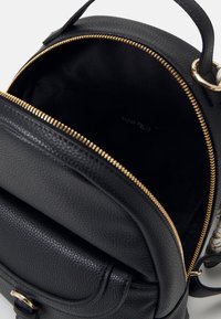 Schwarzer Rucksack aus strukturiertem Leder mit goldenen Reißverschluss, Innentasche und Markenlabel. Kompakte runde Form mit zwei Griffen.