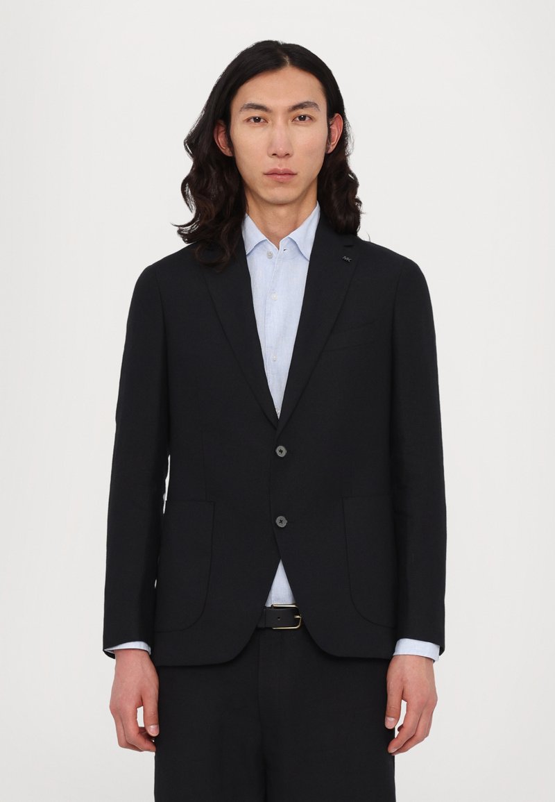 Schwarzer Blazer mit zwei Vorder- taschen, Ein-Knopf-Verschluss, kombiniert mit einem hellblauen Hemd. Auffällige glatte Textur und taillierte Passform.