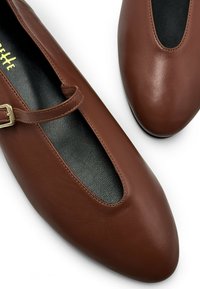 Ballet flats in pelle marrone con punta affilata, design a ritaglio e una sottile fascia con una fibbia dorata. Soletta nera testurizzata visibile.