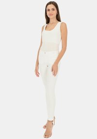Biały bezrękawnik i białe dopasowane dżinsy o gładkiej teksturze; jasnobeżowe szpilki. Minimalistyczny design z delikatnymi detalami logo.