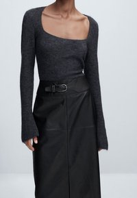 Haut gris en maille à manches longues avec un col carré, associé à une jupe en cuir noire taille haute avec ceinture et fente à l'avant.