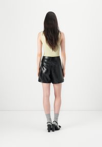 Svarta shorts i konstläder med slät yta och veckad fåll. Kombineras med en ljusgrön ärmlös topp och grå strumpor.