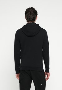 Μαύρο φούτερ με κουκούλα και κορδόνι, με ριμπ μανσέτες και τελείωμα. Το μαλακό ύφασμα έχει λεία υφή και απλό, αδιάκοπο πίσω σχέδιο.